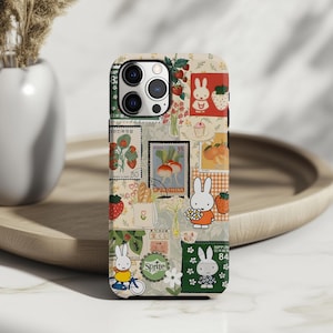 May include: A phone case with a collage design featuring a white rabbit, strawberries, flowers, and vintage stamps. The case has a cream background and a variety of colors, including red, green, and yellow.