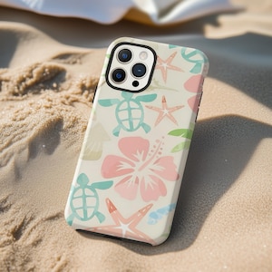 May include: A phone case with a tropical design featuring sea turtles, starfish, and hibiscus flowers in pastel colors. The case is on a sandy surface, suggesting a beach theme.