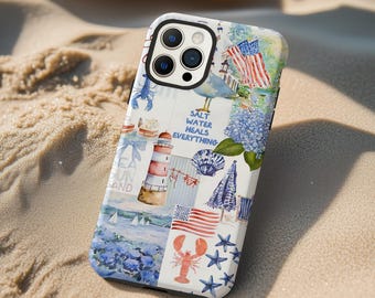 May include: A white and blue phone case with a coastal theme. The case features illustrations of a lighthouse, American flags, a lobster, and the text "Salt Water Heals Everything". The case is on a sandy surface.