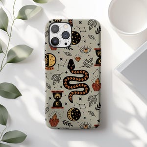 May include: A phone case with a repeating pattern of mystical symbols. The design includes a black and orange snake, moons, stars, crystals, eyes, and leaves on a light gray background. The case has a camera cutout and is likely for a smartphone.