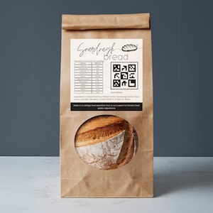 May include: A brown paper bag with a white label that says "Sourdough Bread". The label includes a QR code, nutrition facts, and a list of ingredients. The bag also has a picture of a loaf of sourdough bread.