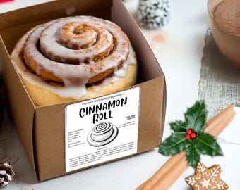 May include: A cinnamon roll with a white frosting and a sprinkle of cinnamon on top. The roll is in a brown cardboard box with a white label that says "Cinnamon Roll" and includes information about the ingredients and Florida's food safety regulations.