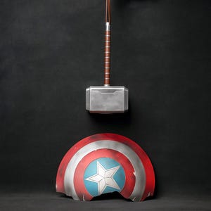 May include: A silver hammer with a brown handle hangs above a red, white, and blue shield with a white star. The shield is slightly damaged. The items are set against a black background.