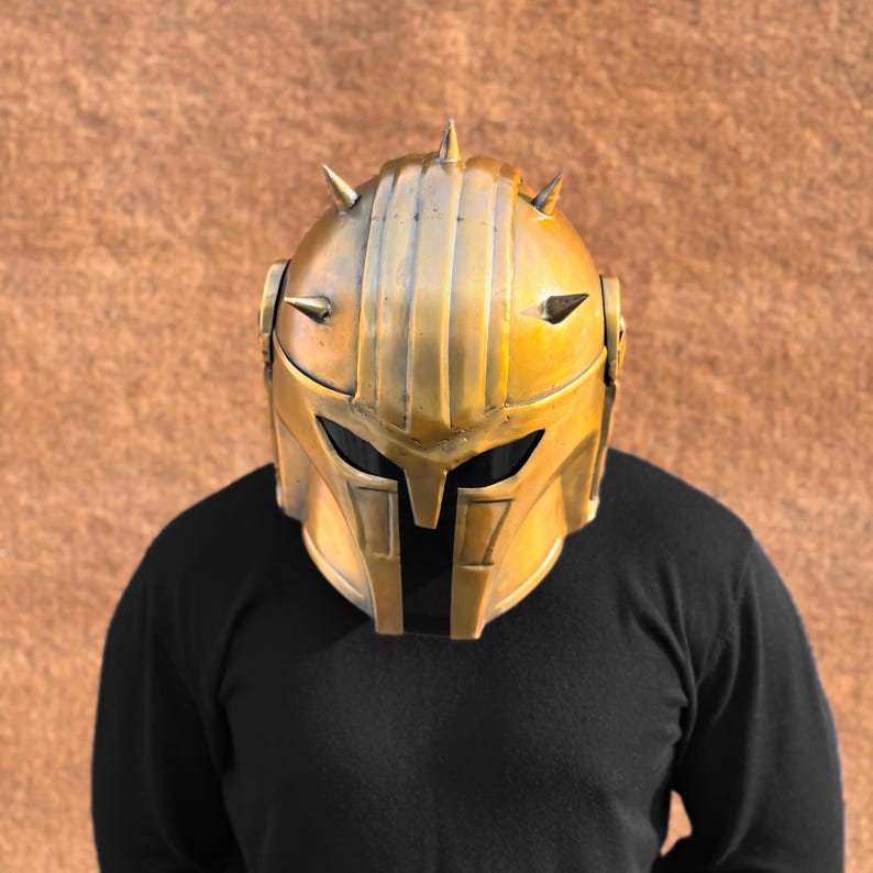 May include: A gold helmet with spikes and a black visor. The helmet has a textured surface and a detailed design.