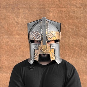 Peut inclure: Un casque en argent et or avec un masque facial et des détails complexes. Le casque est porté par une personne avec une barbe et une chemise noire.