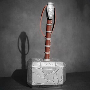May include: A silver and brown hammer with a leather strap. The hammerhead is silver with a cracked stone design. The handle is brown with silver bands and a leather strap. The hammer is a replica of Thor's hammer.
