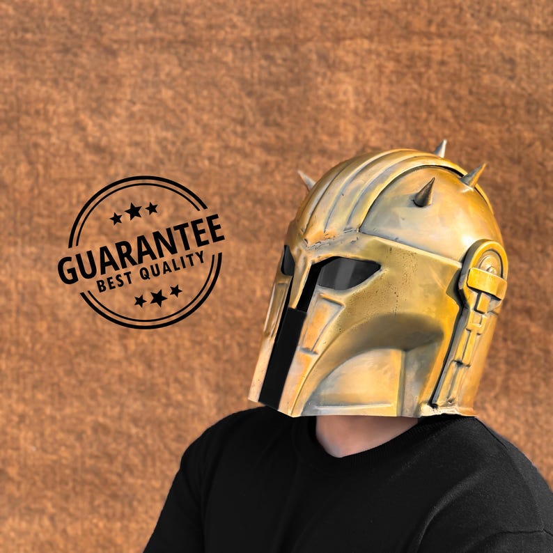 May include: A gold-colored helmet with a black visor and spikes on top. The helmet is worn by a person wearing a black shirt.