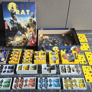Pode incluir: Jogo de tabuleiro "First Rat" com uma caixa com uma ilustração de uma cidade noturna. O jogo inclui cartas amarelas em forma de queijo, peças de jogo em bandejas e um tabuleiro.