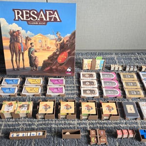 Può includere: Un set completo del gioco da tavolo "Resafa" di Vladimír Suchý. Il gioco include una scatola con un'illustrazione colorata di una scena nel deserto, una varietà di carte, gettoni e altri componenti di gioco.