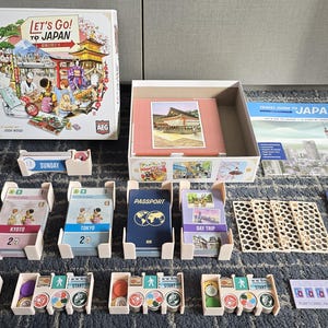 Puede incluir: Un juego de mesa llamado "Let's Go! To Japan" con una caja colorida, un tablero de juego y varias piezas de juego. El juego presenta un mapa de Japón, un pasaporte y otros elementos con temática de viajes.
