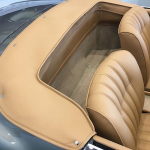Może przedstawiać: Wnętrze klasycznego samochodu z otwieranym dachem. Siedzenia i dach są w jasnym odcieniu brązu, kontrastującym z szarym nadwoziem. Siedzenia mają żebrowany wz&oacute;r, a dach jest zszyty.