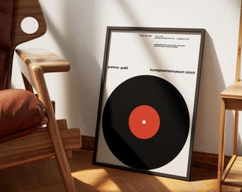 May include: A black and white poster featuring a black vinyl record with a red centre. The poster has the text "grammo - grafik" and "kunstgewerbemuseum zürich" printed on it.