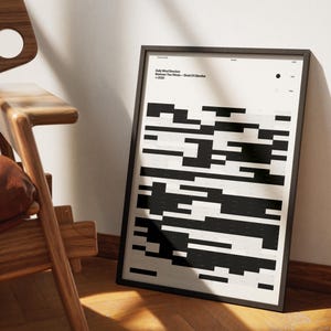 Könnte beinhalten: Ein gerahmter Kunstdruck mit einem schwarz-weißen abstrakten Design. Das Kunstwerk zeigt horizontale und vertikale schwarze rechteckige Formen auf cremefarbenem Hintergrund. Der Rahmen ist schwarz. Der Druck lehnt an einer Wand neben einem Holzstuhl.