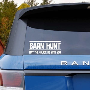 May include: A blue SUV with a white vinyl sticker on the back window that reads "Barn Hunt, May the Course Be With You". The SUV is parked in front of a red barn with white trim.