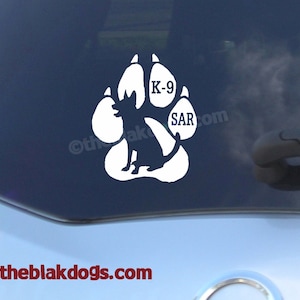 May include: White vinyl decal of a dog paw print with a silhouette of a dog sitting inside the print. The words "K-9" and "SAR" are inside the paw print.