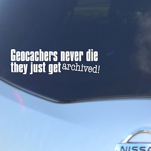 May include: A white vinyl sticker on the back window of a silver car. The sticker says "Geocachers never die they just get archived!"