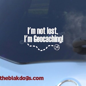 May include: White vinyl decal for a car window. The decal says "I'm not lost, I'm Geocaching!" with a dashed line and a compass symbol.