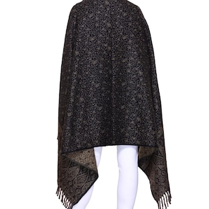 May include: A black shawl with a paisley pattern and fringe. The shawl is draped over a person's shoulders and is worn with white trousers.