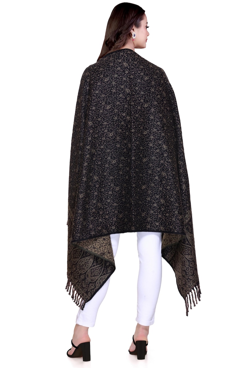 May include: A black shawl with a paisley pattern and fringe. The shawl is draped over a person's shoulders and is worn with white trousers.