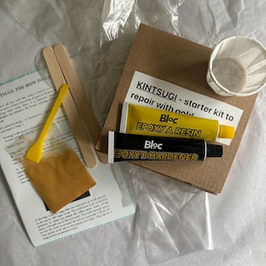 Puede incluir: Kit de reparación Kintsugi con resina epoxi dorada y endurecedor, dos palitos de madera, una taza pequeña y un paquete de polvo dorado. El kit incluye instrucciones sobre cómo reparar la cerámica rota con oro.