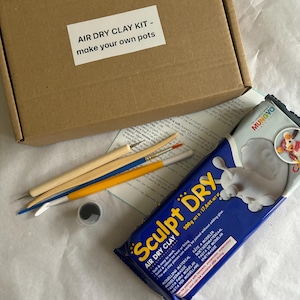 Könnte beinhalten: Ein Bastelset zur Herstellung von Töpfen, mit einem Karton mit der Aufschrift "AIR DRY CLAY KIT - make your own pots". Enthält eine 500g Packung lufttrocknenden Ton, Bildhauerwerkzeuge und einen kleinen Behälter.