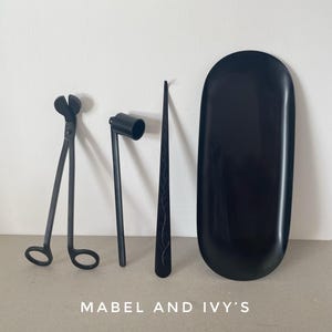K&ouml;nnte beinhalten: Ein Set schwarzer Kerzenpflegewerkzeuge, bestehend aus einer Wickelschere, einem Docht-Tauchwerkzeug, einem Docht-Aufkleber und einem schwarzen Tablett. Mabel and Ivy's.