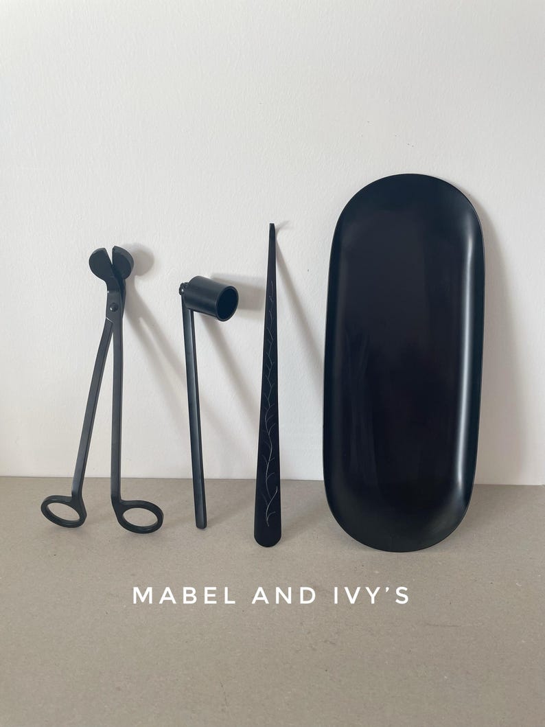 K&ouml;nnte beinhalten: Ein Set schwarzer Kerzenpflegewerkzeuge, bestehend aus einer Wickelschere, einem Docht-Tauchwerkzeug, einem Docht-Aufkleber und einem schwarzen Tablett. Mabel and Ivy's.