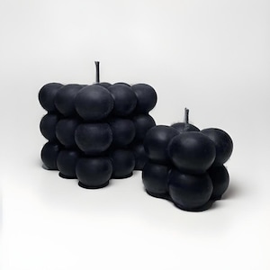 May include: Two black bubble candles, one larger than the other, on a white background. The candles are made of multiple round shapes that resemble bubbles.