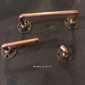 May include: Three copper pipe towel racks with black flanges. The flanges have the text "MABEL & IVY'S" and numbers on them.