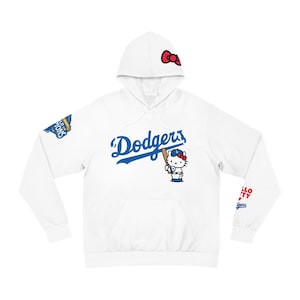 Op de afbeelding: Witte hoodie met het Los Angeles Dodgers-logo in blauwe letters en een Hello Kitty honkbalspeler-afbeelding. De capuchon heeft een rode strik en de mouwen hebben teamgraphics. Een kangoeroezak is zichtbaar.