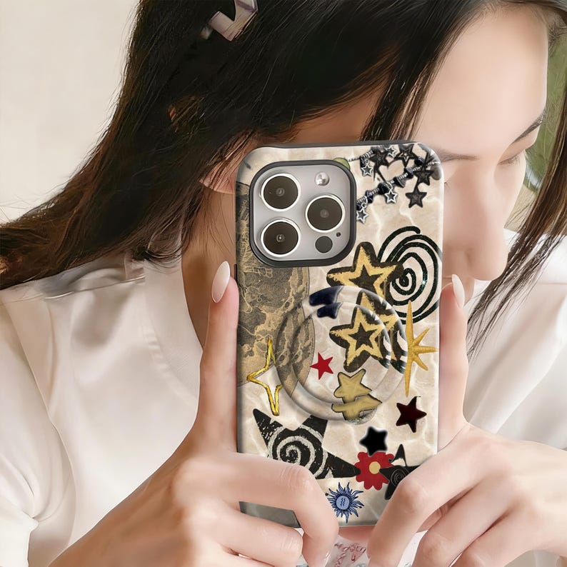 May include: A phone case with a cream-colored background and a collage of stars, swirls, and other decorative elements in gold, black, red, and blue. The case has a camera cutout.