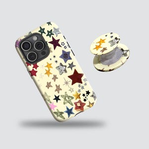 May include: A cream-coloured phone case and matching phone grip, both decorated with a pattern of colourful stars in various sizes and designs. The phone case has a camera cutout and the grip is extended.