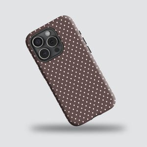 May include: A brown phone case featuring a pattern of small white polka dots. The case has a black camera module and buttons on the side. The phone case is designed to fit a smartphone.