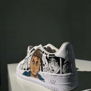 K&ouml;nnte beinhalten: Wei&szlig;e Low-Top-Sneaker mit einer schwarz-wei&szlig;en Manga-Illustration von Charakteren aus dem Anime Attack on Titan. Die Sneaker haben das Wort "AIR" an der Seite.