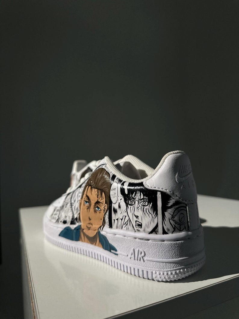 K&ouml;nnte beinhalten: Wei&szlig;e Low-Top-Sneaker mit einer schwarz-wei&szlig;en Manga-Illustration von Charakteren aus dem Anime Attack on Titan. Die Sneaker haben das Wort "AIR" an der Seite.