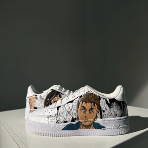 K&ouml;nnte beinhalten: Wei&szlig;e Sneaker mit einem individuellen Design, das Charaktere aus dem Anime Attack on Titan zeigt. Das Design beinhaltet Schwarzwei&szlig;-Manga-Panels und eine Nahaufnahme eines Gesichts. Das Wort "AIR" ist an der Seite des Schuhs aufgedruckt.