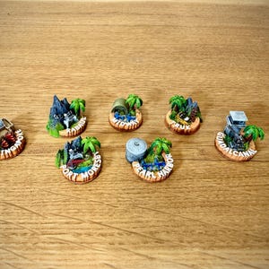 Könnte beinhalten: Eine Sammlung von Miniatur-Souvenirmagneten mit tropischen Inselmotiven. Jeder Magnet hat eine kreisförmige Basis mit einem detaillierten Diorama von Sehenswürdigkeiten, Palmen und Text. Die Magnete sind auf einer Holzoberfläche angeordnet.