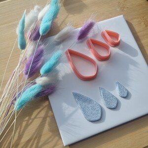 May include: A set of four pink teardrop-shaped cookie cutters and three gray teardrop-shaped cookies.