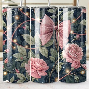May include: A floral tumbler with a dark blue background, featuring pink roses, leaves, and a large pink bow. The design includes string lights and a straw. The tumbler is designed for cold beverages.