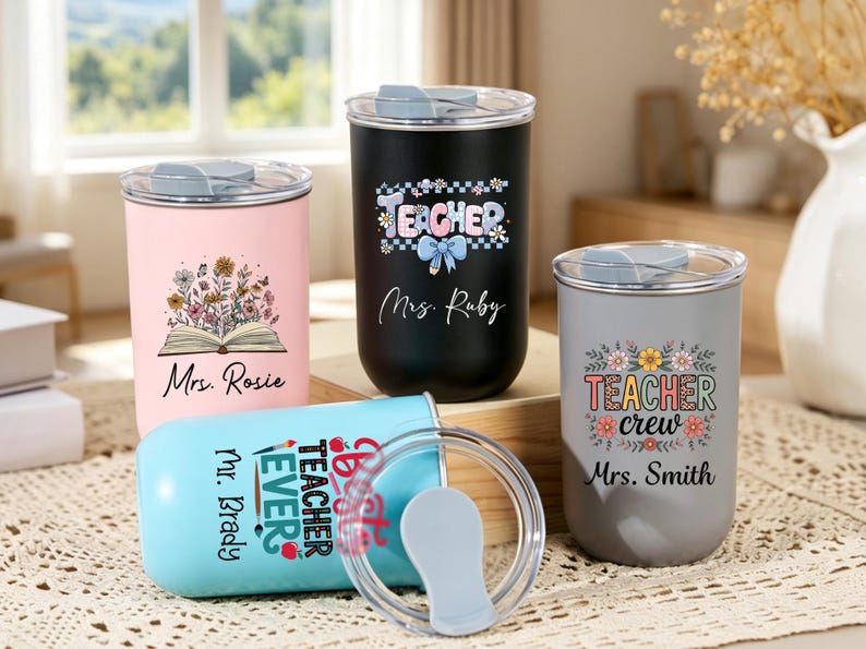 May include: Four cylindrical tumblers with clear lids, featuring personalized text and floral graphics. Colors include pink, black, light blue, and gray. Text includes "Mrs. Rosie," "Teacher Mrs. Ruby," "Best Teacher Ever Mr. Brady," and "Teacher crew Mrs. Smith."