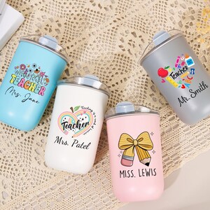 May include: Four stainless steel tumblers with clear lids in light blue, white, gray, and pink. Each features a unique teacher-themed graphic with school supplies and personalized names: Mrs. Jane, Mrs. Patel, Mr. Smith, and Miss. Lewis.