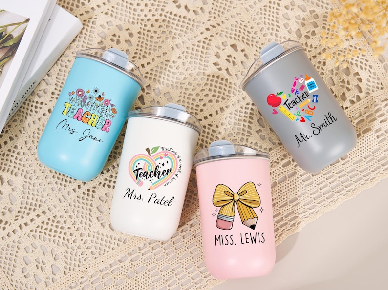 May include: Four stainless steel tumblers with clear lids in light blue, white, gray, and pink. Each features a unique teacher-themed graphic with school supplies and personalized names: Mrs. Jane, Mrs. Patel, Mr. Smith, and Miss. Lewis.