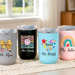 May include: Four cylindrical tumblers with clear lids, each featuring unique teacher-themed graphics and names. The gray tumbler shows a pencil bow, the black one has a smiley face, the light blue one displays school supplies, and the pink one a rainbow.