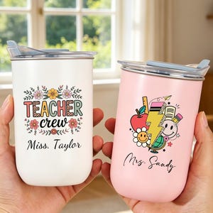 May include: Two stainless steel tumblers with lids. The white tumbler features floral accents, the text "TEACHER crew," and the name "Miss. Taylor." The pink tumbler displays school-themed graphics, a lightning bolt, and the name "Mrs. Sandy."