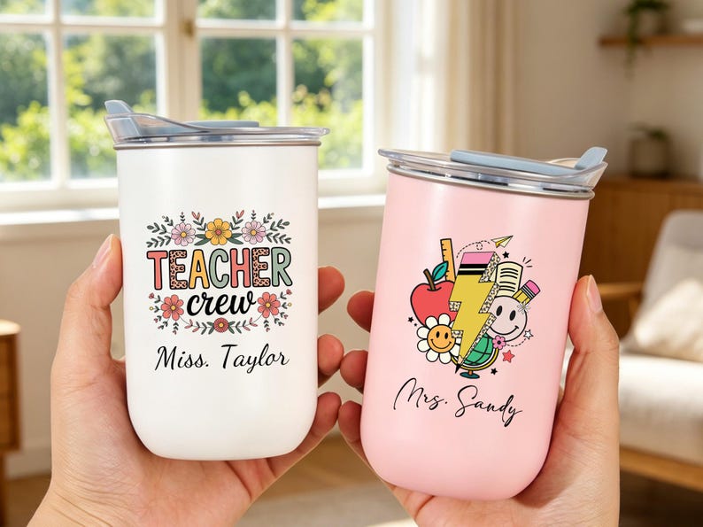 May include: Two stainless steel tumblers with lids. The white tumbler features floral accents, the text "TEACHER crew," and the name "Miss. Taylor." The pink tumbler displays school-themed graphics, a lightning bolt, and the name "Mrs. Sandy."