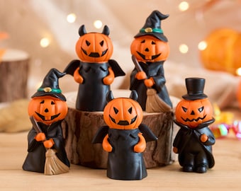 May include: A collection of Halloween-themed figurines. Each figurine features an orange pumpkin head with a carved face, dressed in black cloaks and hats. Some hold brooms or have devil horns. The figurines are arranged on a wooden surface.