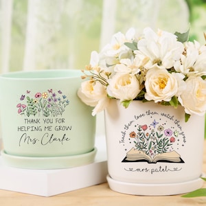 May include: Two ceramic flower pots, one mint green and one white, with floral designs and text. The green pot says "Thank You For Helping Me Grow Mrs. Clarke." The white pot says "Teach them, love them, watch them grow mrs. patel."