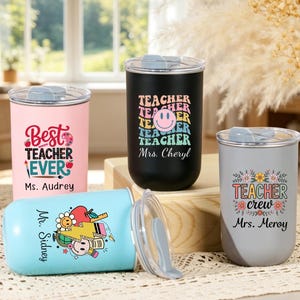 May include: Four stainless steel tumblers with clear lids. One pink tumbler reads Best Teacher Ever Ms. Audrey. One black tumbler features a smiley face and the text Teacher Mrs. Cheryl. One gray tumbler says Teacher crew Mrs. Meroy. One light blue tumbler says Mr. Sidney.