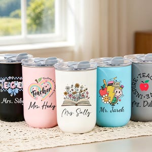 May include: Five cylindrical tumblers with lids in black, light pink, white, light blue, and gray. Each features unique teacher-themed graphics, including flowers, apples, and pencils, with personalized names like Mrs. Siby, Mrs. Hedy, Mrs. Sally, Mr. Jarek, and Mr. Duke.