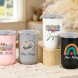 May include: Four cylindrical tumblers with clear lids, each featuring unique teacher-themed graphics and names. The colors include pastel pink, light gray, white, and matte black. Each tumbler displays custom text such as Mrs. Belen, Miss. Chaya, Joyce, and Mrs. Nicky.